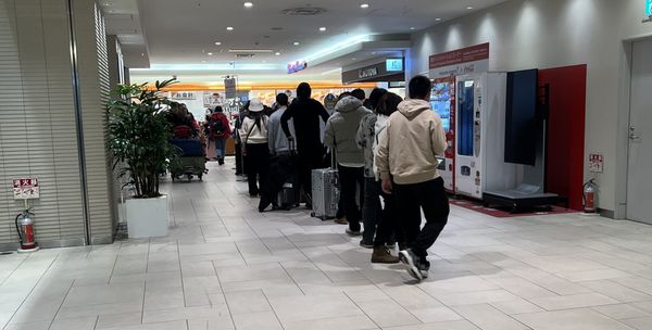 A long queue of travellers with suitcases winding past the shops inside New Chitose Airport