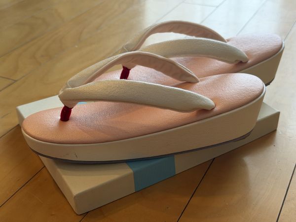 Made-to-measure zori from Gion Naito seen from the side, pink top and white sides, resting on the shop's box