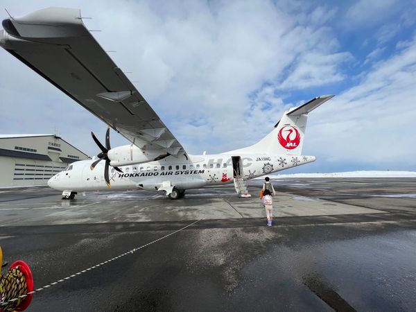A Hokkaido Air System ATR 42 on a wet snow-edged apron with passengers boarding