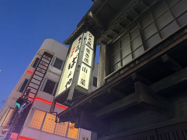 Illuminated vertical sign of the izakaya Ban-ya in Hachinohe, Aomori, at dusk, listing hie-meshi, grilled fish and mountain v