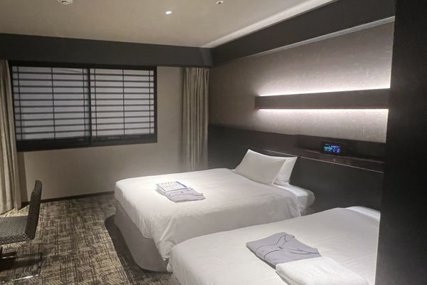A Japanese hotel twin room with two separate single beds, each made up with its own duvet, in a narrow room
