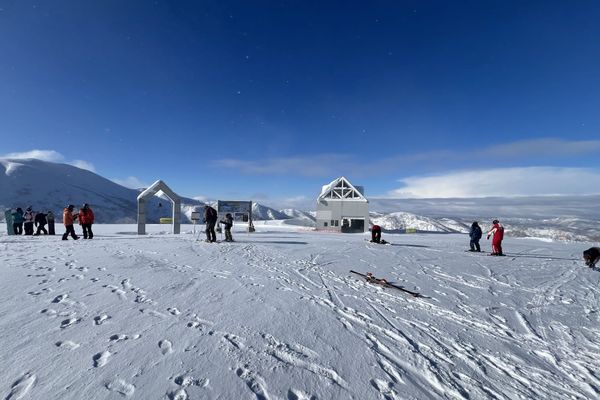 Wide open snow at Kiroro under a blue sky, with a low base building and a few skiers