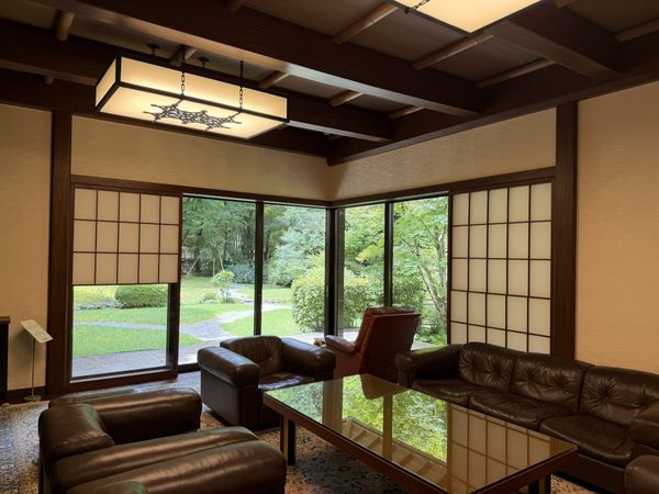 The drawing room of the Former Kishi Residence in Gotemba: brown leather sofas under a bamboo ceiling, with shoji panels beside a window onto the garden