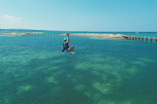 Clear turquoise water over a reef in Okinawa with a long pier running out from the shore