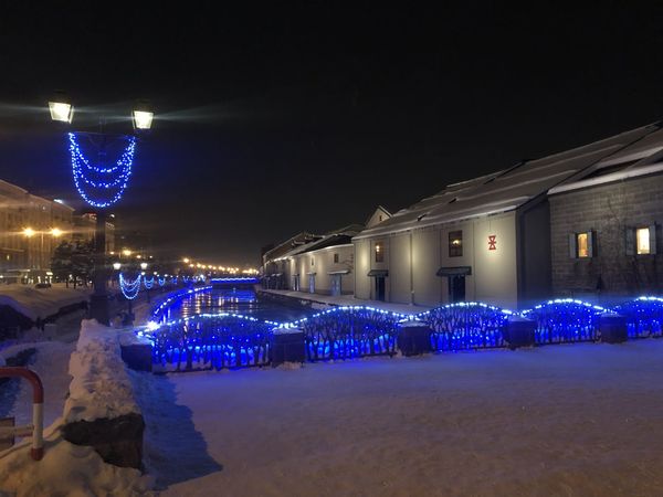 Otaru canal warehouses lit blue at night with snow along the promenade