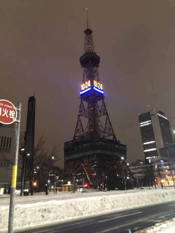 Sapporo TV Tower above roadside snowbanks on Odori at night