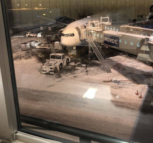 A Boeing 787 at a jet bridge on a snow-covered stand at New Chitose Airport at night