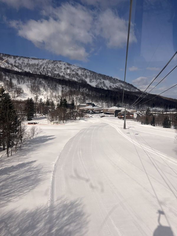 A groomed run seen from a chairlift, forested slopes on both sides