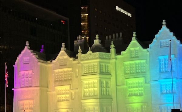 A large snow sculpture of a historic building lit in shifting colours at night