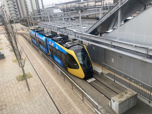 A yellow Utsunomiya Light Line tram waiting at the Utsunomiya Station East terminus platform, seen from the elevated walkway