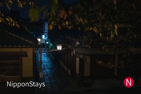 Stone-paved lane in Kyoto's Higashiyama district at night, lined with wooden walls and lantern light