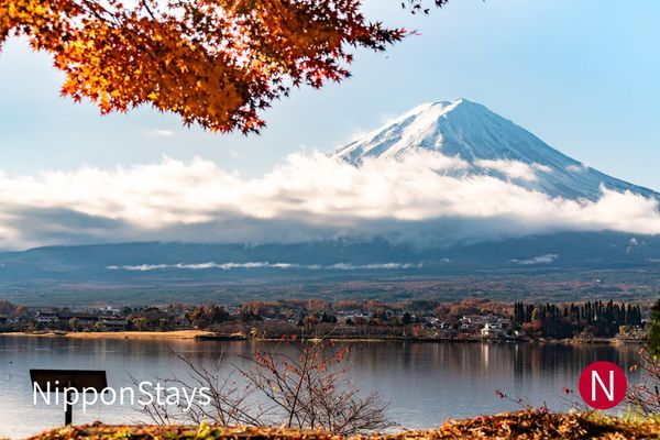 Mount Fuji seen across a lake, framed by red maple branches