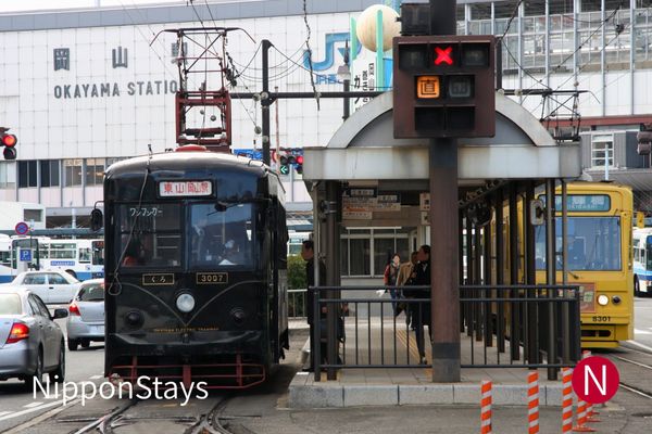 A tram waiting at the stop outside Okayama Station