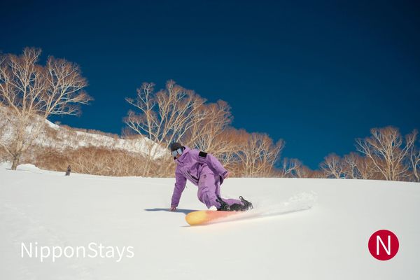 A snowboarder carving a turn on an open slope at Hakuba