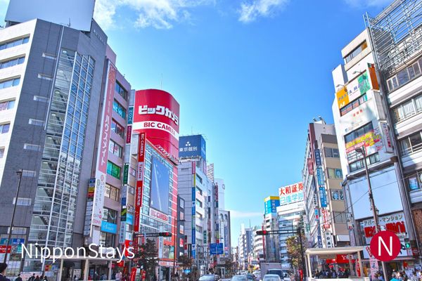 A daytime street in Ikebukuro with shop signage on both sides