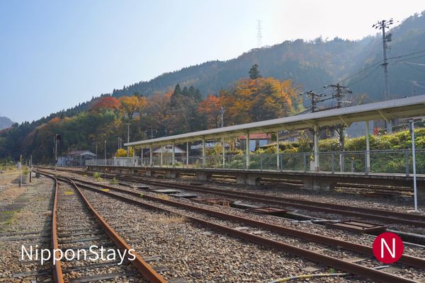 An empty rural station platform and tracks with autumn-coloured hills behind