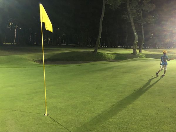A child walking up a floodlit green at night on the Tom Watson Golf Course, long shadow cast ahead