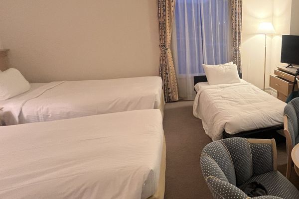 Two fixed twin beds beside a third, lower bed on a dark folding frame, set up by the window in a hotel room sold for three guests