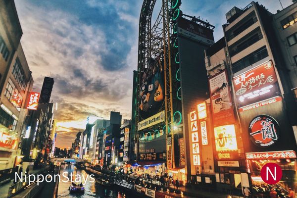 Dotonbori canal at dusk with a ferris wheel and illuminated restaurant signs above the water
