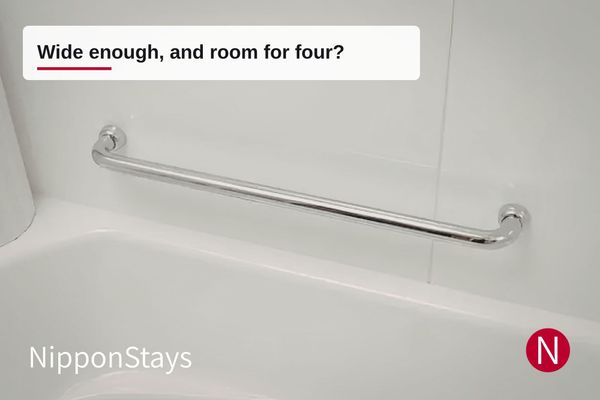 A stainless steel grab bar fixed to the wall beside a white bathtub