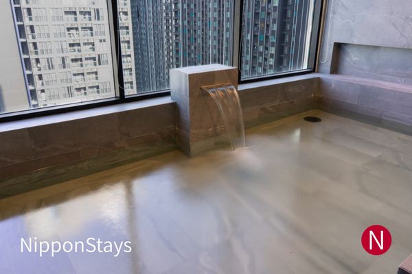 Hotel public bath with a stone spout pouring into the tub beside floor-to-ceiling windows