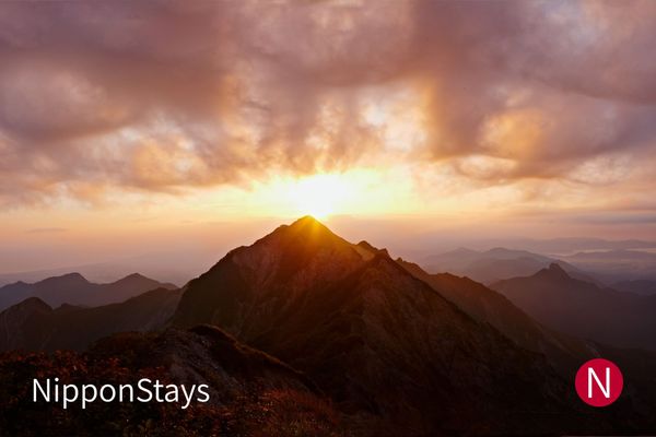 The sun rising behind a sharp mountain peak above a sea of clouds, seen from a summit