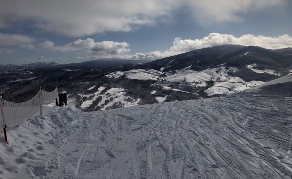 A safety net on red poles running along the edge of a groomed run at a Hokkaido ski area, with the valley and neighbouring pe