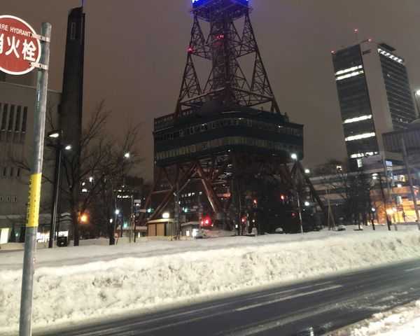 Sapporo TV Tower lit at night above a plowed snowbank beside a cleared street