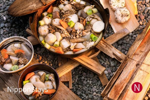 A pot of imoni with taro, mushrooms and carrot cooking beside a riverbank