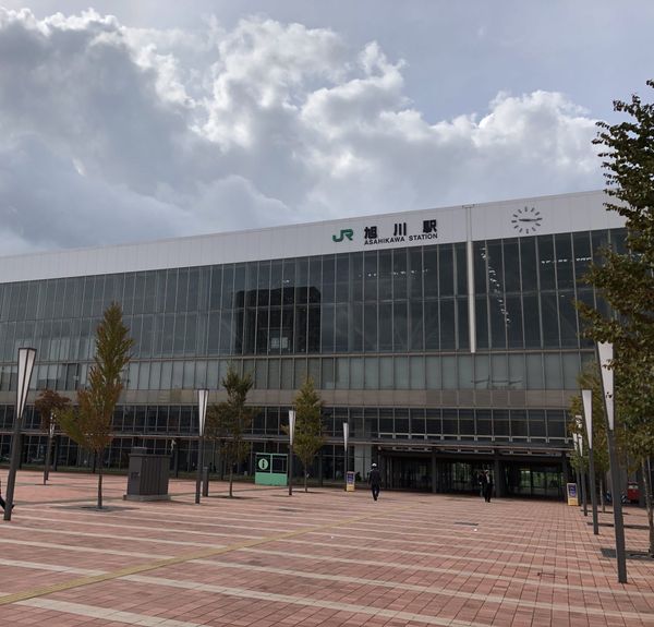 The glass facade of JR Asahikawa Station in Hokkaido under a cloudy sky, seen from the brick station square