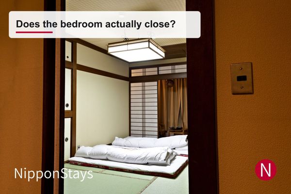 A tatami room with futon laid out, seen through a wooden doorway from the next room