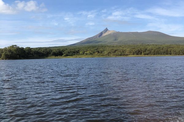 Mount Komagatake rising above the forested shore of Lake Onuma, seen from a boat on the lake