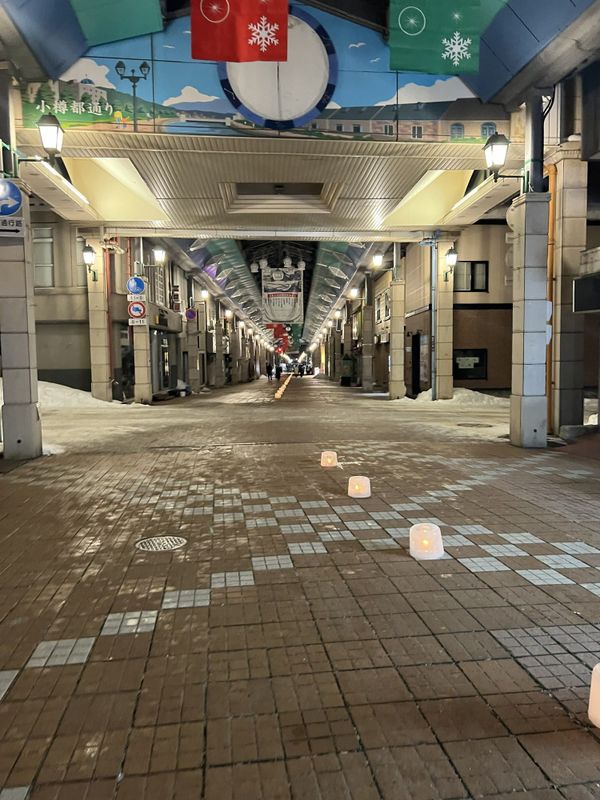 Small ice-candle lanterns lined up down the middle of the Miyakodori shopping arcade in Otaru at night, with snow piled at the edges