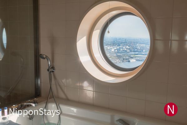 A bathtub beneath a round window looking out over Tokyo Bay