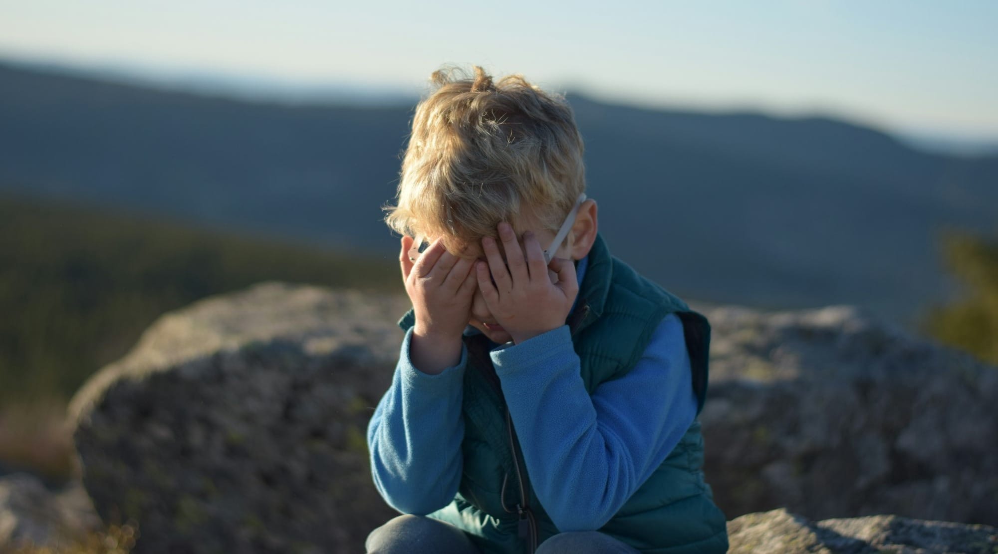 a young boy sitting on top of a large rock
