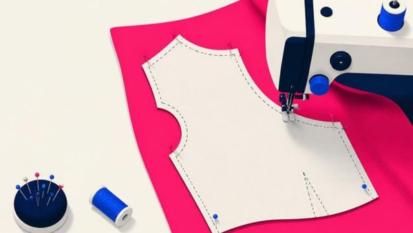 A sewing machine follows the dotted cut line of a paper pattern pinned to pink fabric.