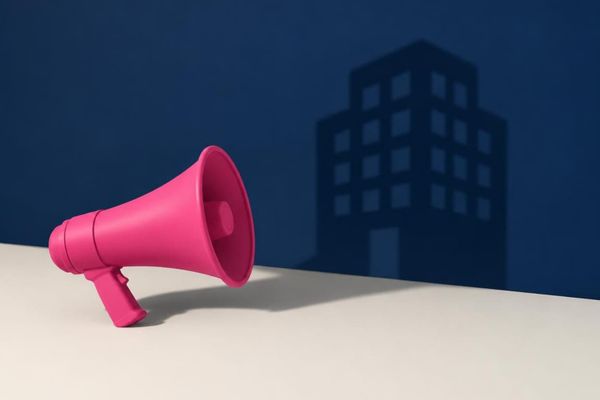 Pink megaphone on a white ledge against a navy wall with the shadow of an office building