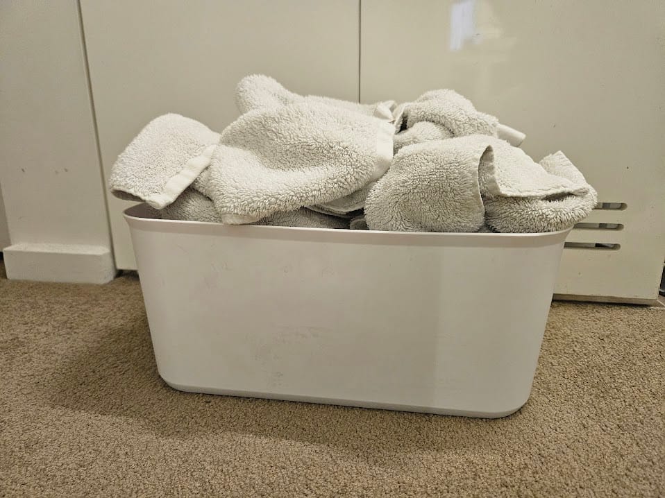 Two clean wicker baskets holding folded towels and organised underwear in a minimalist white bathroom with wood accents