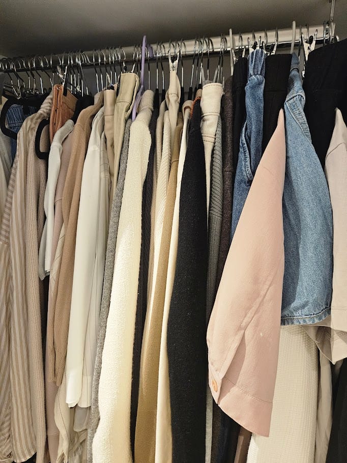 Open minimalist wardrobe with all clothing hung on matching slim velvet hangers in a white bedroom with natural wood flooring