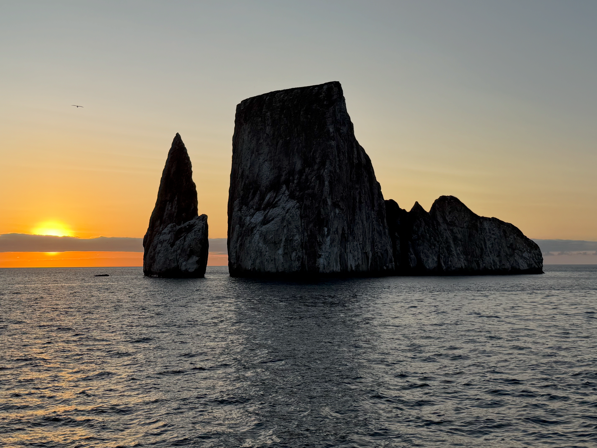 Sunset behind towering volcanic rock formations of Kicker Rock Leon Dormido rising from the ocean in the Galápagos Islands.