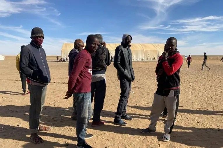 Un groupe de jeunes hommes attendent pour recevoir de la nourriture à Assamaka, après avoir été expulsés d'Algérie, en mars 2