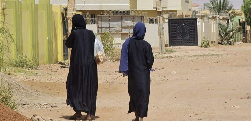 Des femmes, sacs de courses à la main, marchent dans une rue déserte du quartier Jabra à Khartoum. Photo AFP via Getty Images