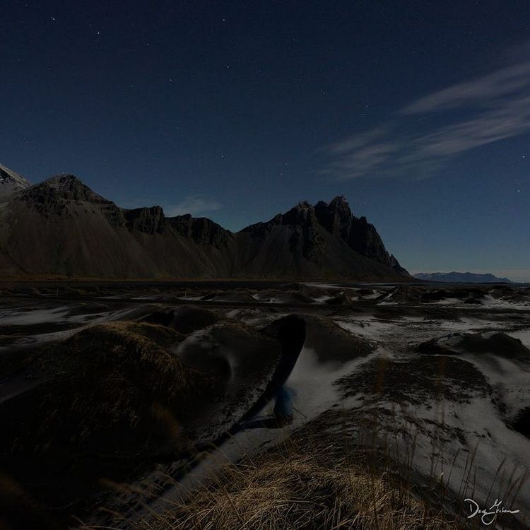a moonlit Icelandic beach with black sand, mountains, and grasses, doppled with ice and snow.
