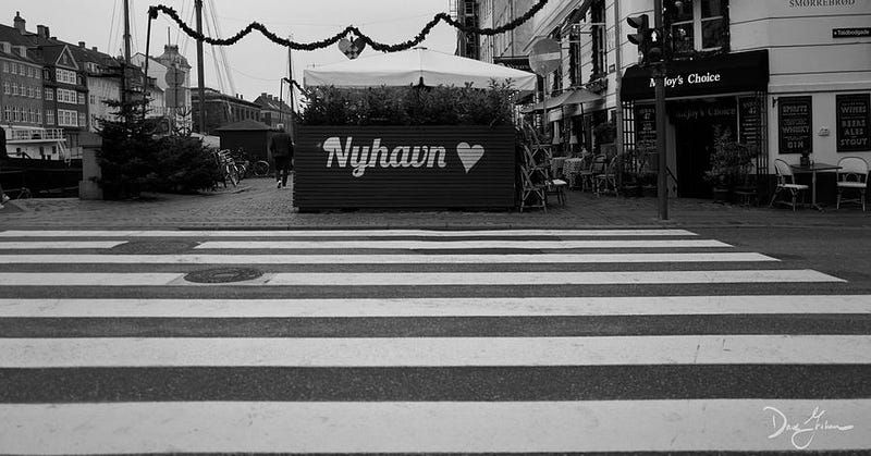 A crosswalk in front of a wooden palisade stating “Nyhavn” with a painted heart.
