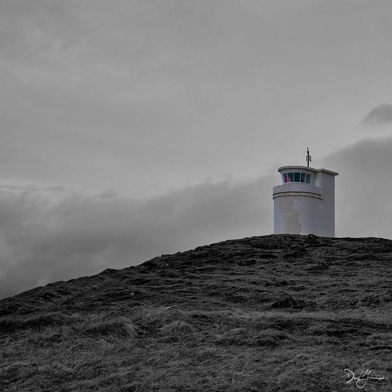 lighthouse in iceland on a bluff overlooking the ocean and grass.