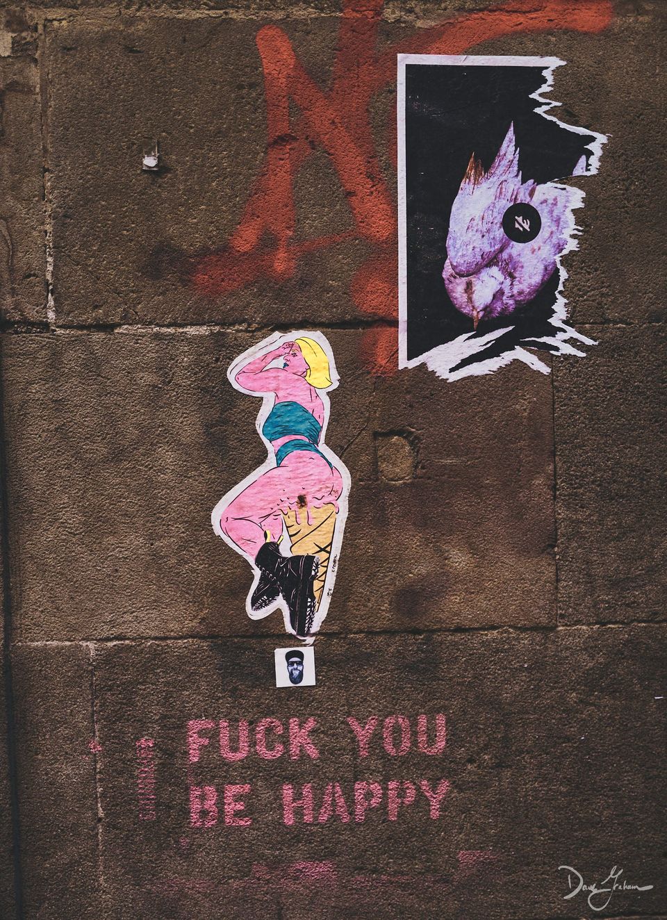 Image of a sticker of a woman plastered to the wall in a Madrid neighbourhood with the words "Fuck you be happy" stenciled underneath