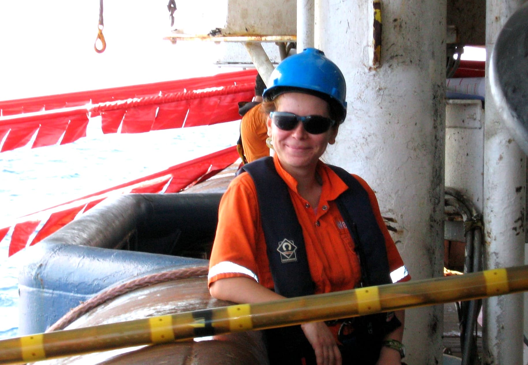 Aurelia Paraschiv smiling on the deck of a vessel at sea, wearing a blue hard hat and a life vest.