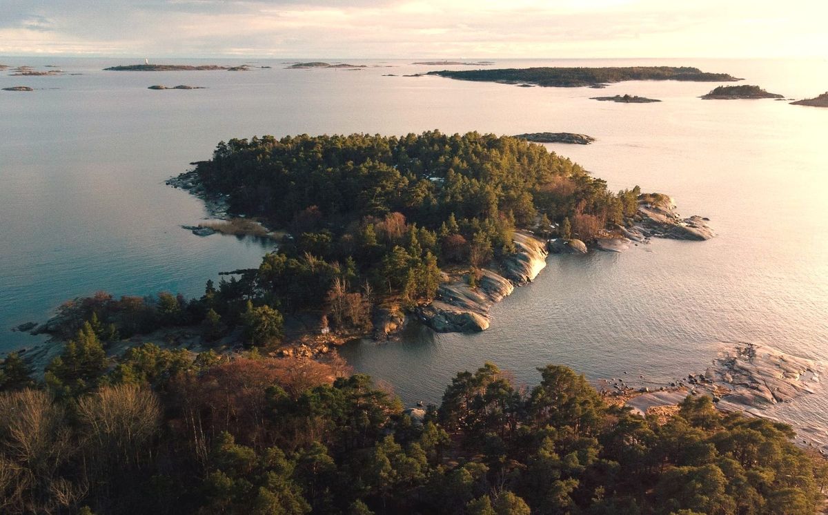Aerial view of pine-covered islands and smooth granite rocks in a calm sea at sunset.