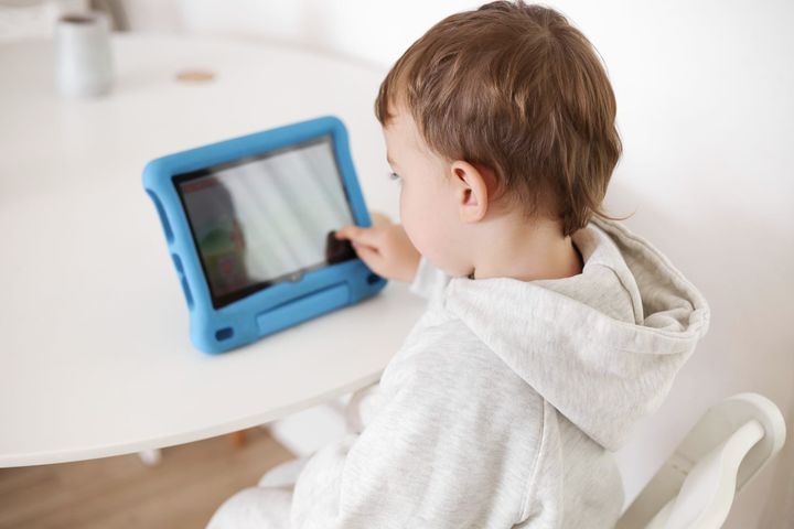 Toddler boy touching the screen of a blue-cased tablet propped on a table, illustrating mindful screen time for young children