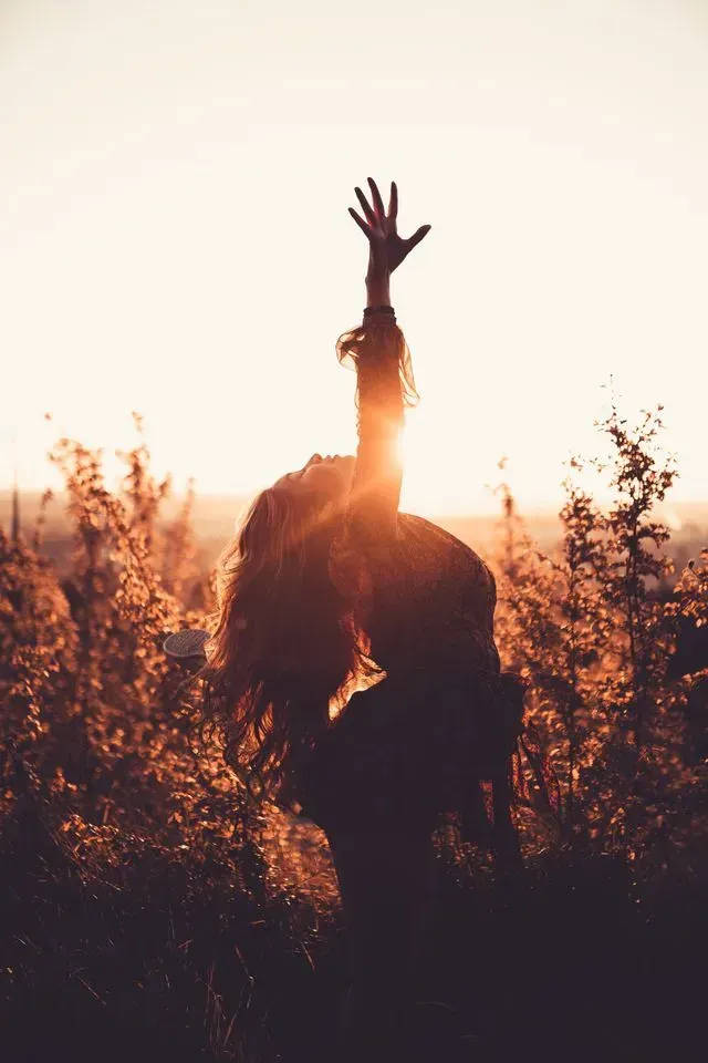 A happy, free woman celebrating financial freedom at sunset, representing budgeting and enjoying life.